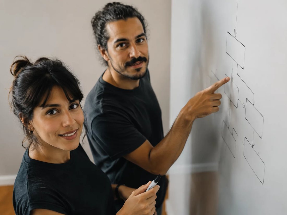 Dois alunos em pé diante do quadro branco, desenhando a ordem de um argumento